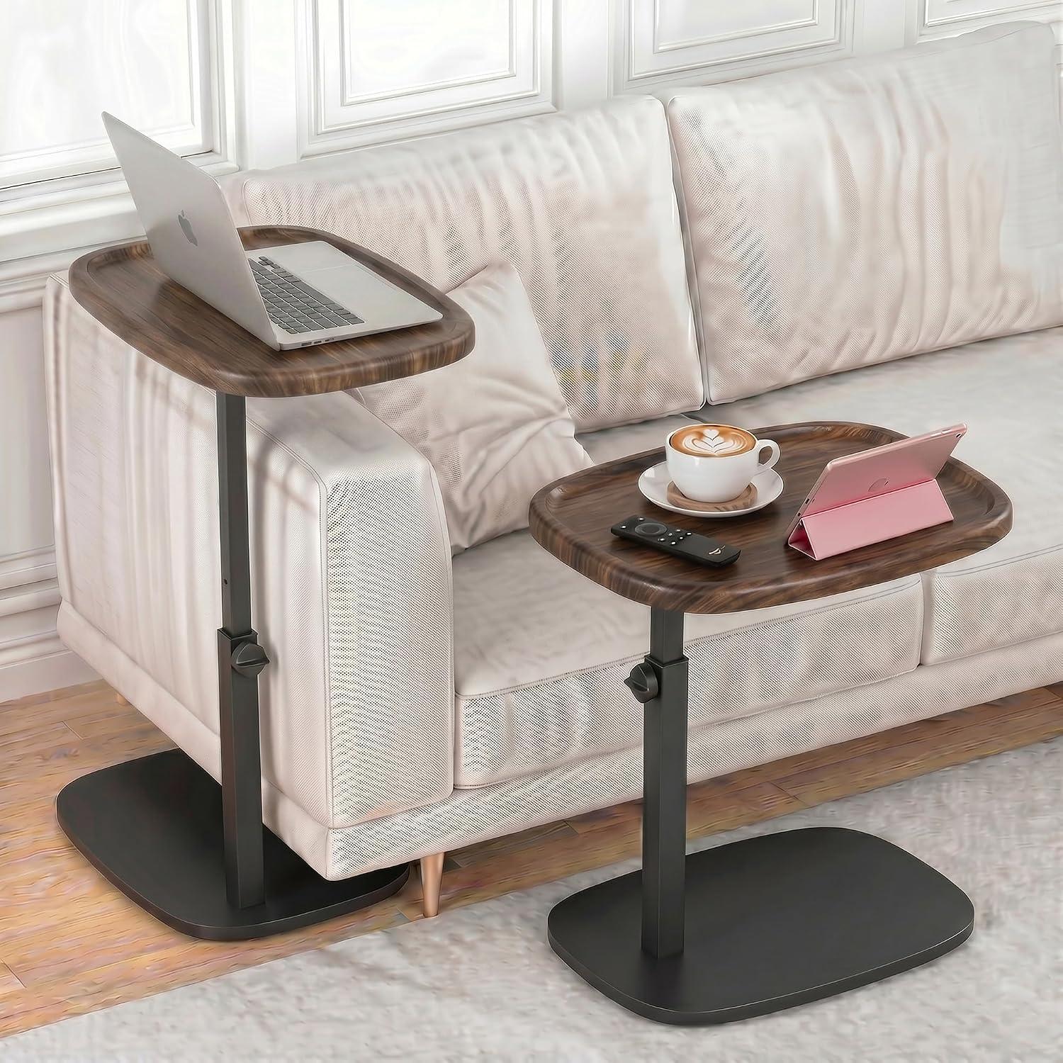 Walnut and black adjustable C side tables styled beside a cream sofa with a laptop, coffee cup, tablet, and remote in bright neutral living room light.