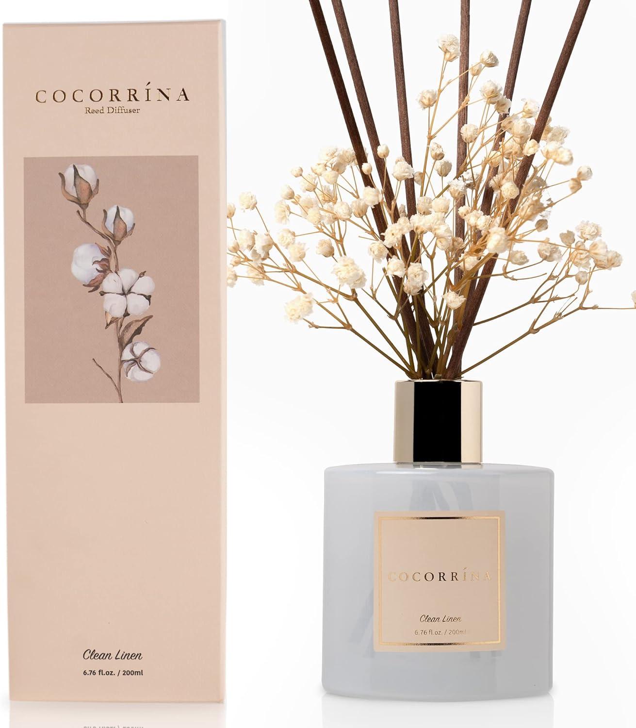 Frosted glass bathroom reed diffuser with dark reeds and dried white florals styled on a bright shelf with neutral decor and soft natural light.