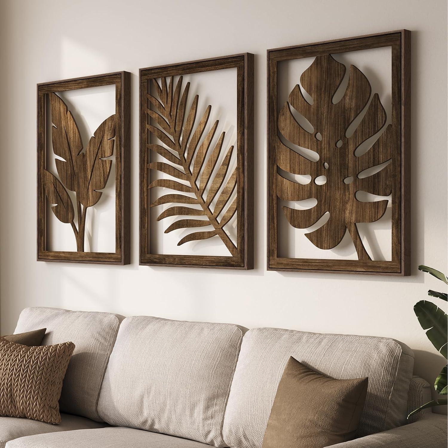 Three carved wood botanical wall art panels above a cream linen sofa with neutral pillows, warm natural light, and a potted plant for boho living room decor.