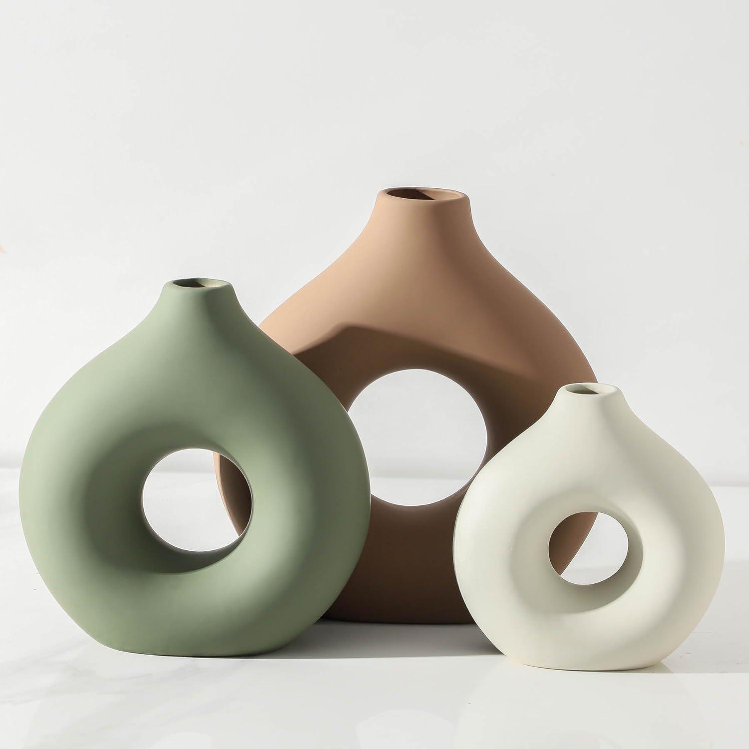 Three sculptural ceramic vases in sage green, terracotta brown, and cream styled on a bright shelf with soft neutral minimalist decor
