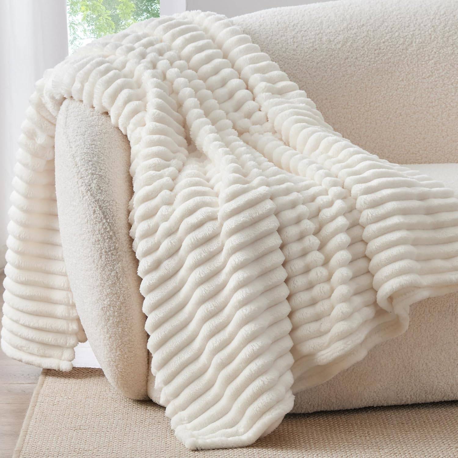 Cream white ribbed fleece throw blanket draped over a boucle couch in bright natural light, styled for soft neutral living room decor.