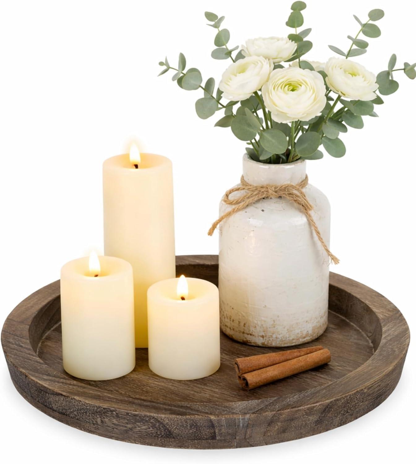 Round distressed wood tray styled with glowing pillar candles, a rustic ceramic vase, white flowers, eucalyptus, and cinnamon sticks for a farmhouse coffee table decor tray.