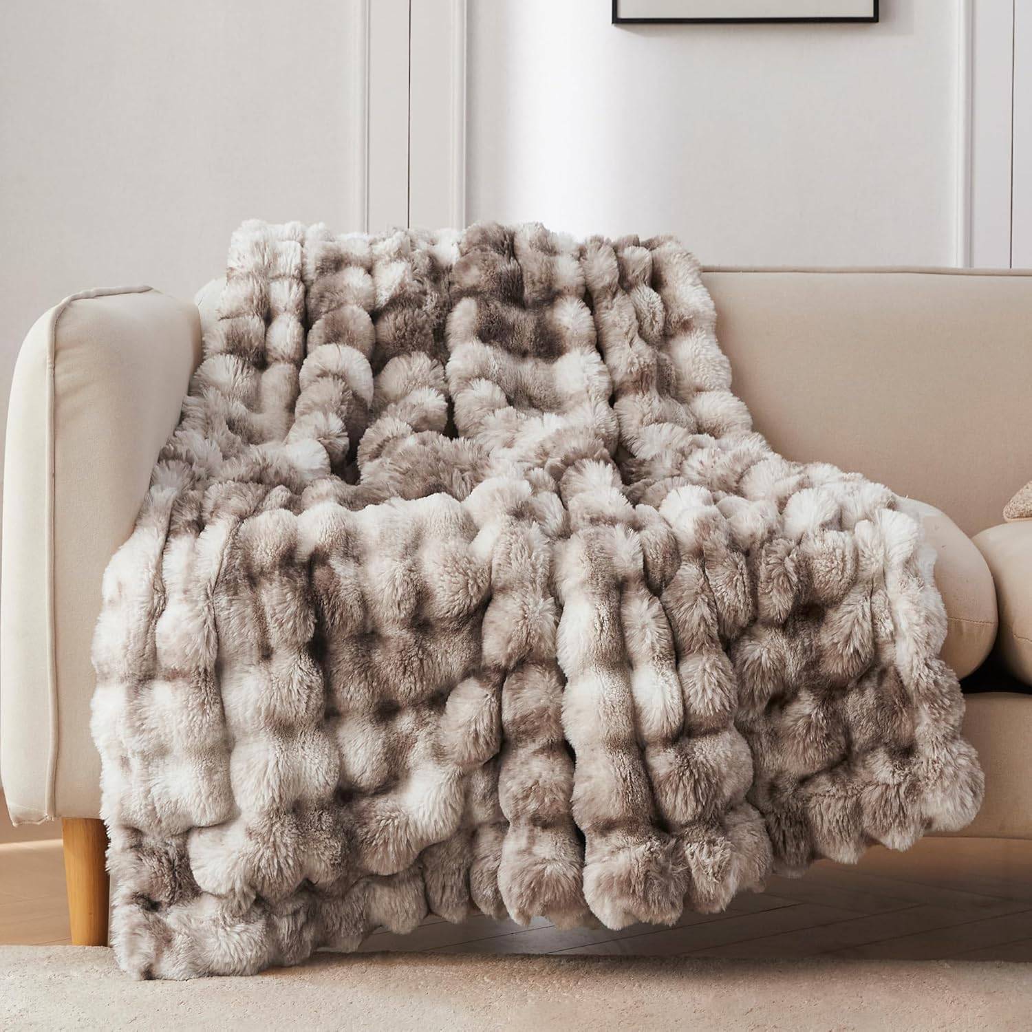 Tie dye brown faux fur throw blanket draped over a beige sofa in a bright neutral living room with plush texture and calm warm decor.