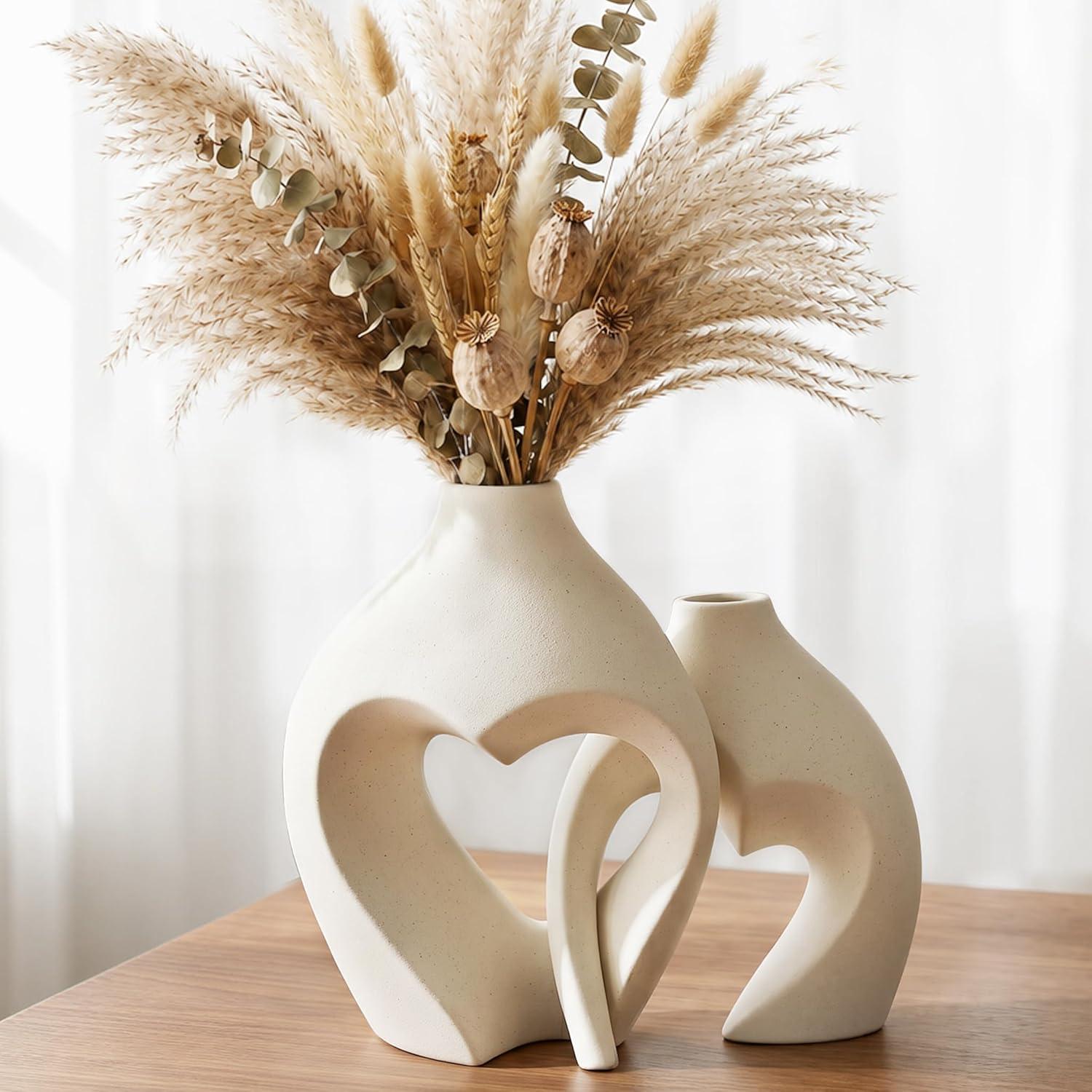 Two white ceramic heart-shaped vases on a wood table with pampas grass and eucalyptus, perfect for neutral boho heart vase decor styling.