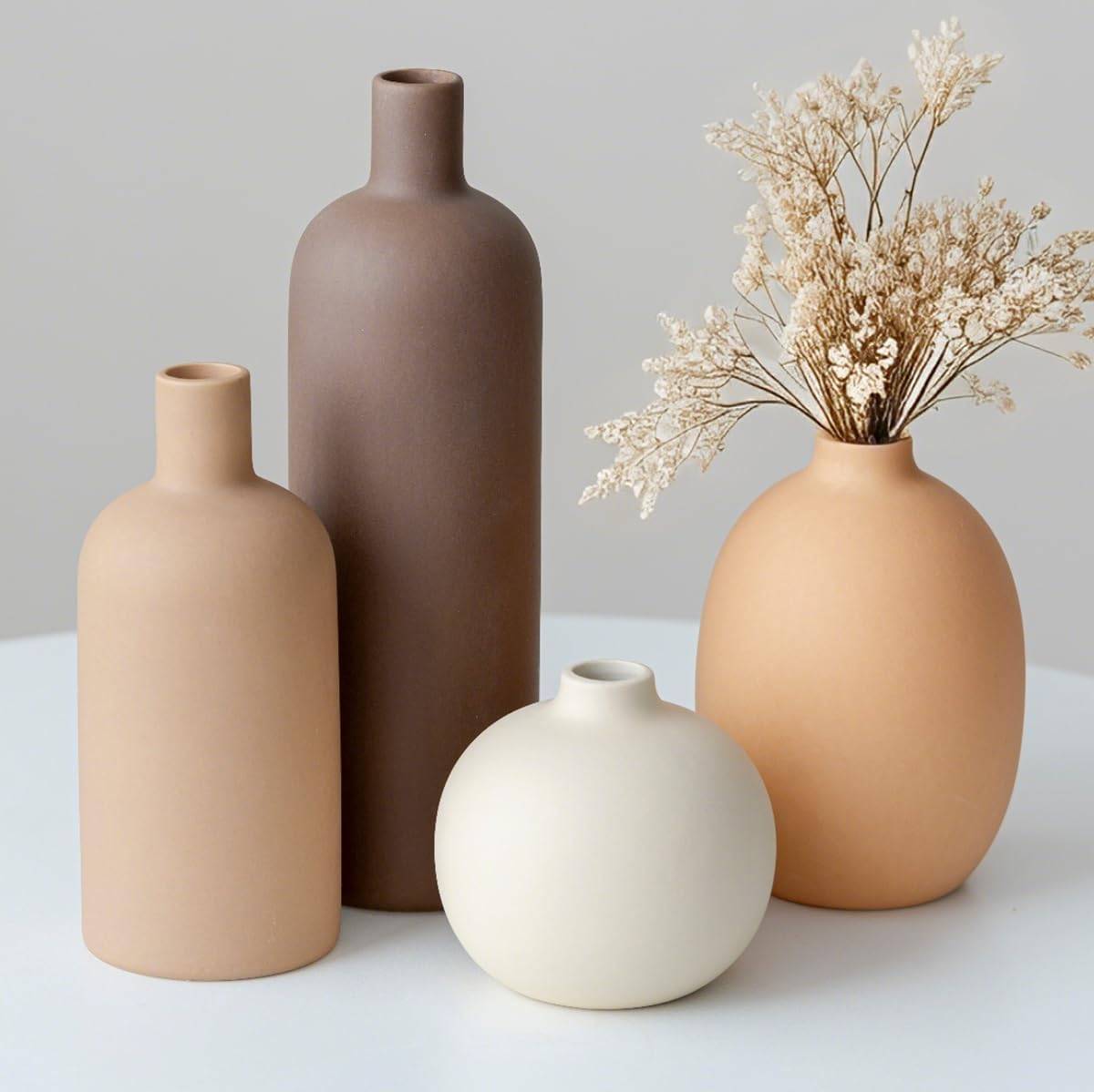 A four-piece modern ceramic vase set in neutral colors styled on a wooden home decor shelf with dried botanicals.