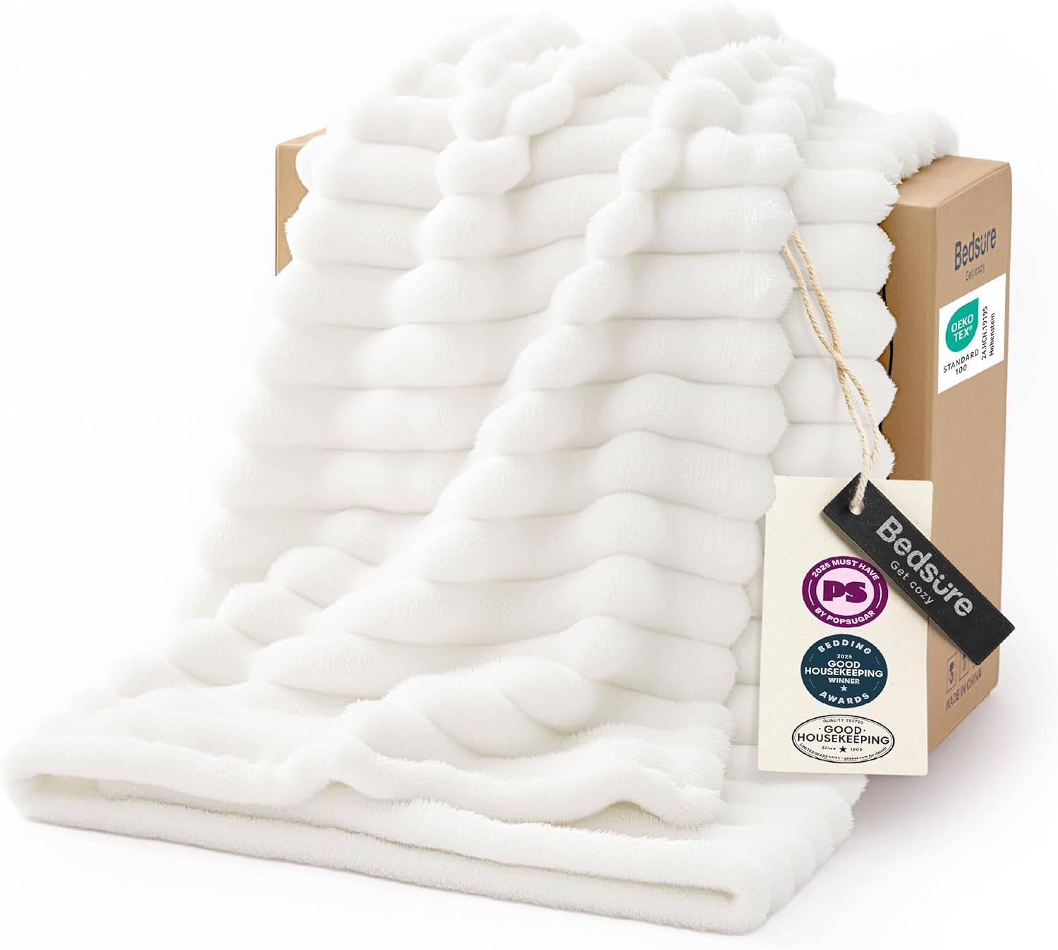 Off-white textured fleece white throw blanket draped from a cardboard gift box on a bright white background, showing plush wavy ridges and soft sofa-ready texture.